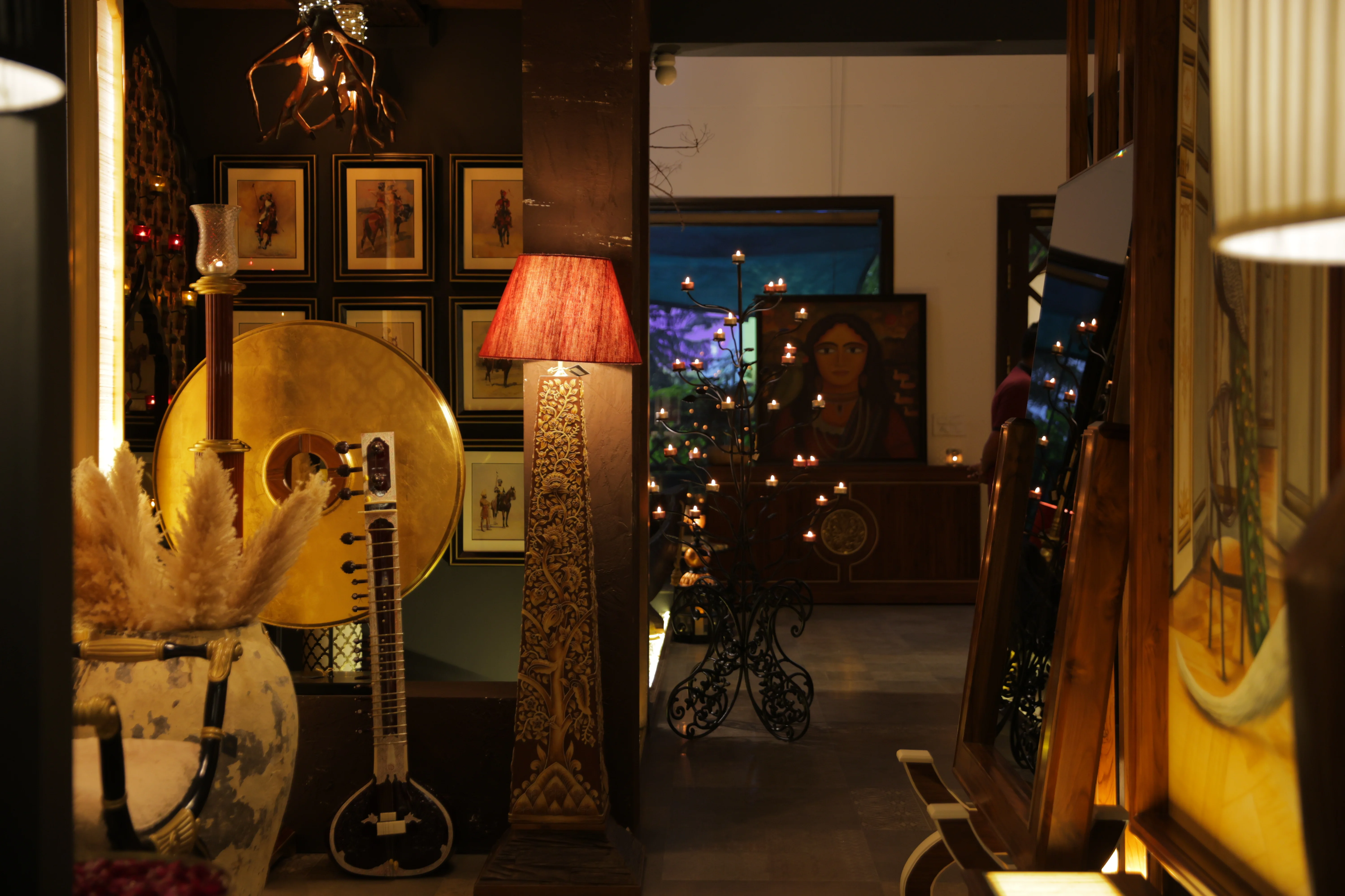 Gallery interior view with warm lighting, framed artwork on walls, and decorative lamp